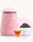 Timebai_yunnan_beauty_black_tea_with_a_pink_tea_canister_loose_leaves_in_a_white_bowl_and_a_glass_cup_of_amber_tea_on_a_white_background.
