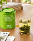 Timebai Orchid Bi Luo Chun Green Tea Tin Beside a Glass of Brewed Green Tea