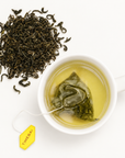 Timebai Orchid Bi Luo Chun Green Tea Brewing in a White Cup Beside Loose Tea Leaves