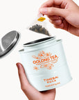 Timebai Pomelo Oolong Tea – Hand Lifting a Pyramid Tea Bag from an Open Tin