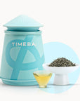 Timebai early spring bi luo chun green tea with a turquoise tea canister, loose leaves in a white bowl, and a glass cup of pale yellow tea on a white background..
