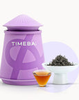 Timebai golden peony black tea with a purple tea canister, loose leaves in a white bowl, and a glass cup of amber tea on a white background.